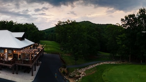A lodge with a deck and outdoor seating, surrounded by a golf course and forested hills. - Massanutten Resort (McGaheysville)