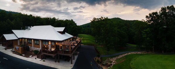 A lodge with a deck and outdoor seating, surrounded by a golf course and forested hills. - Massanutten Resort (McGaheysville)