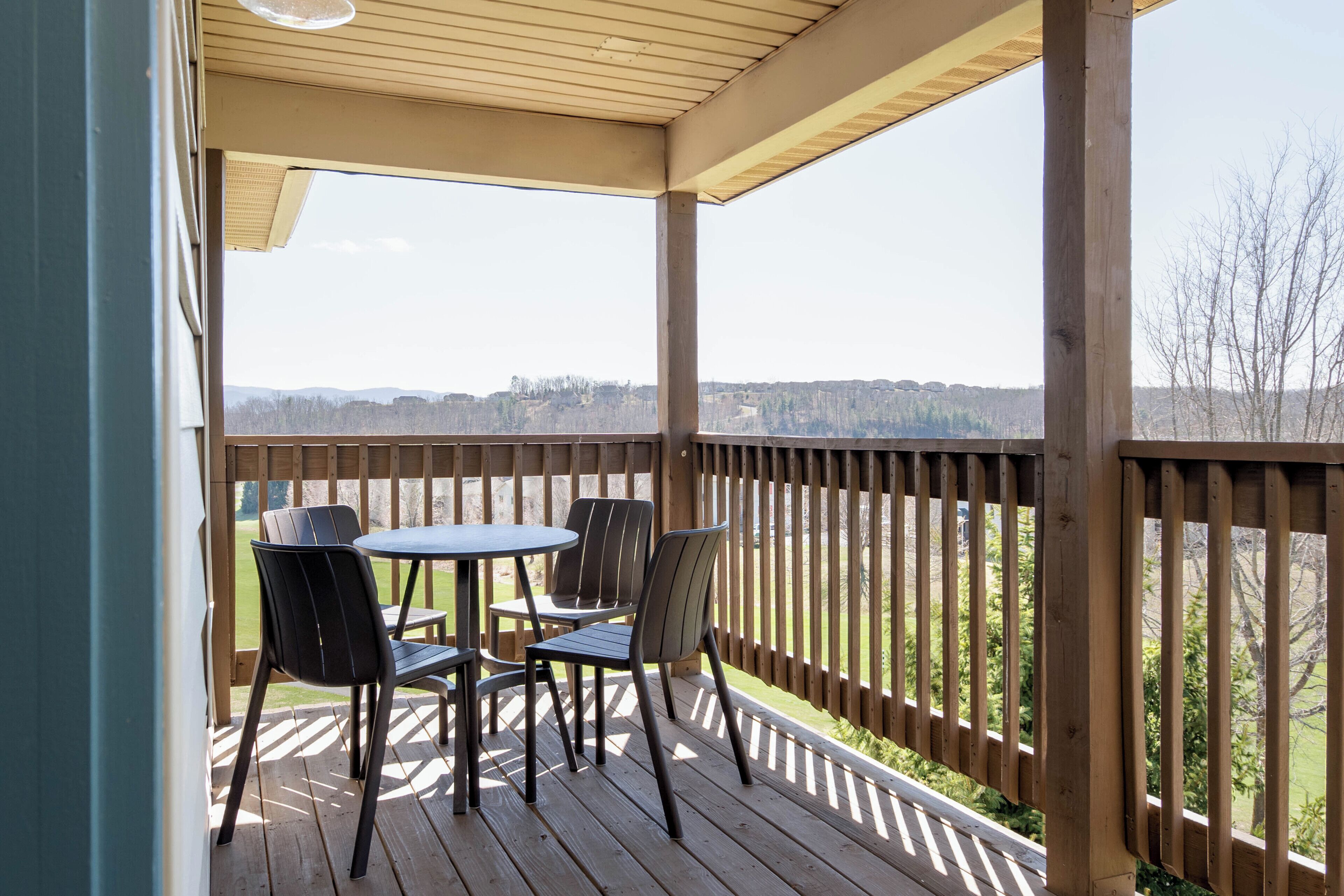 A covered outdoor deck with a table and chairs, a wooden railing, and a view of a distant landscape.