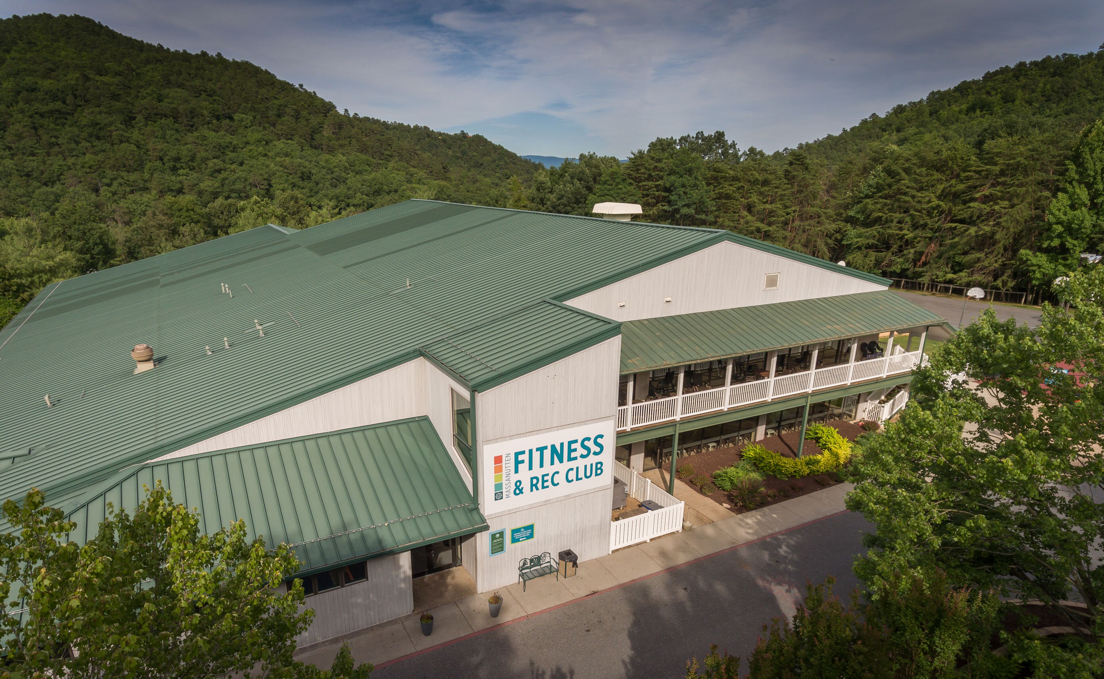 A fitness and recreation club building with a green roof, surrounded by lush greenery and hills.
