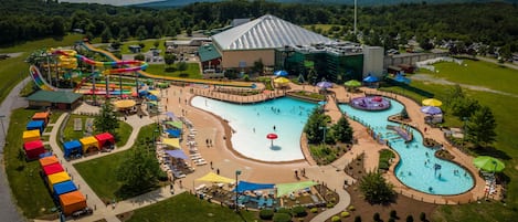 An aerial view of a water park with multiple pools, slides, and a large building with a sloped roof.