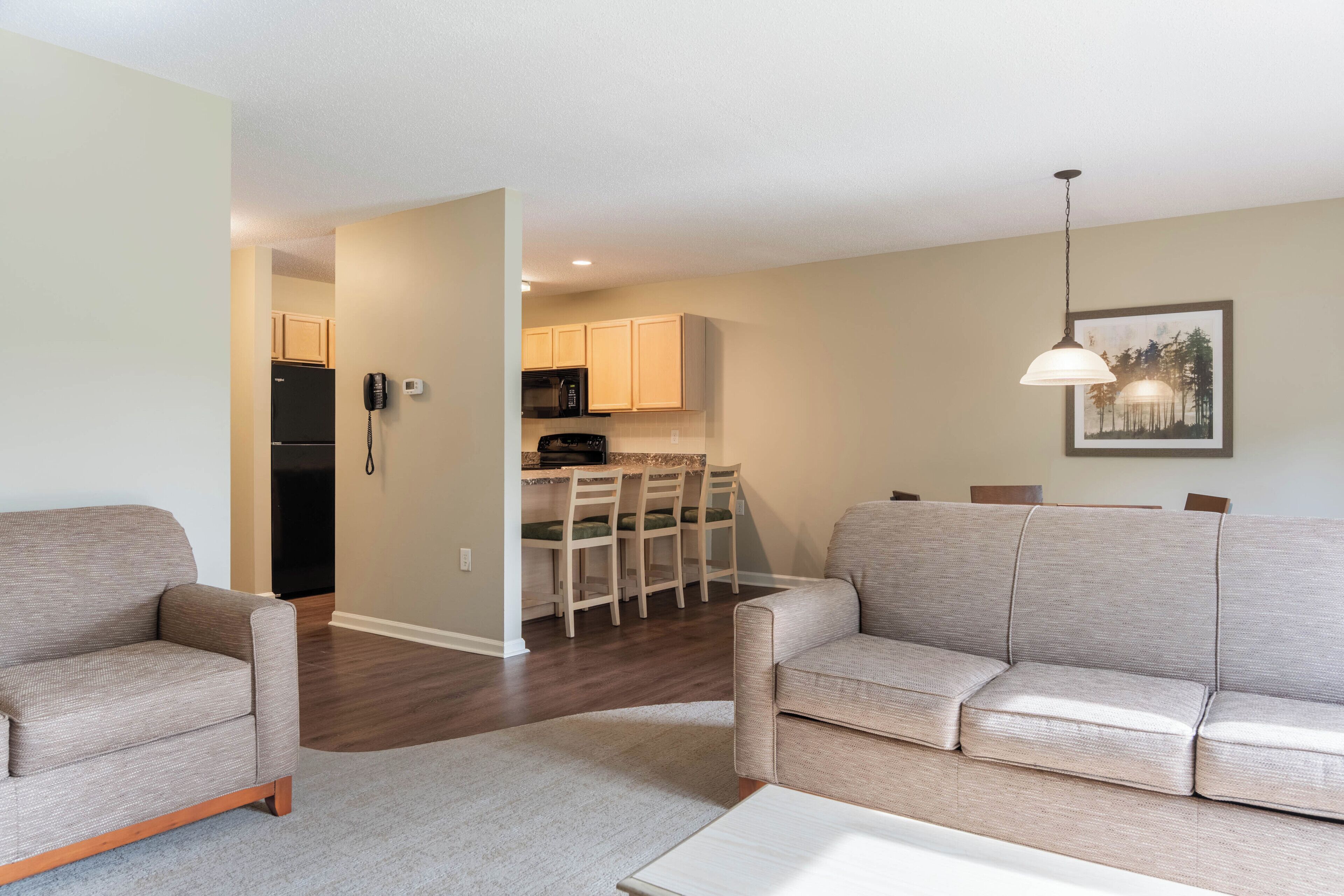A living room with a sofa, a coffee table, and a dining area with chairs and a kitchen in the background.