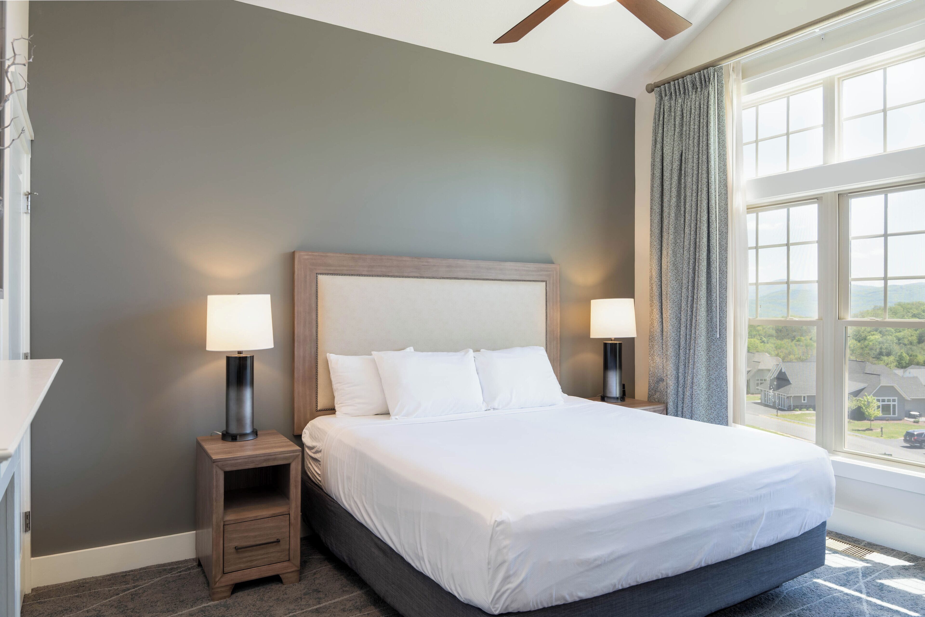 Un dormitorio con una cama grande, dos mesitas de noche con lámparas, una ventana con cortinas y vistas al exterior.