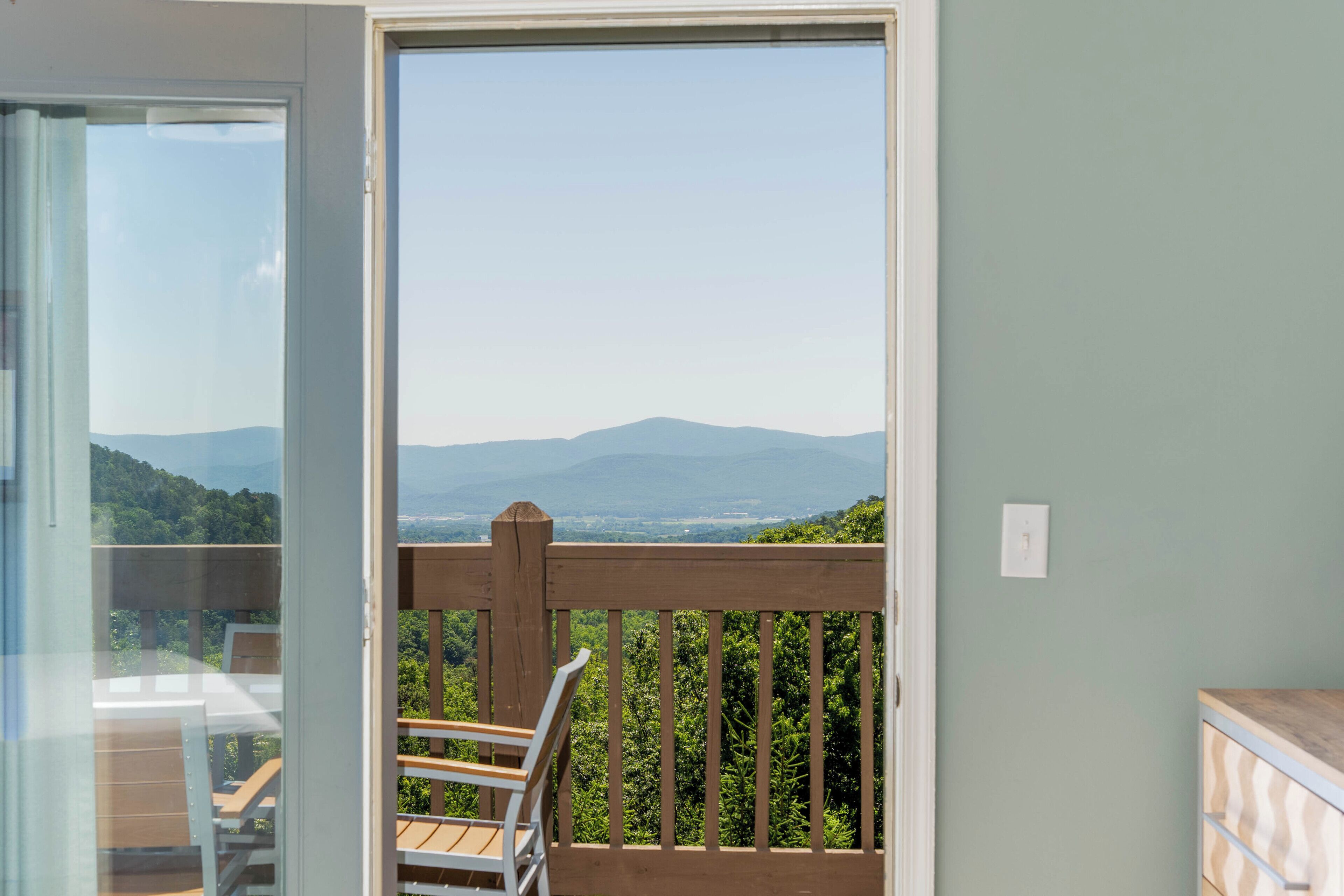 A balcony with a wooden railing, a chair, and a view of a mountainous landscape.
