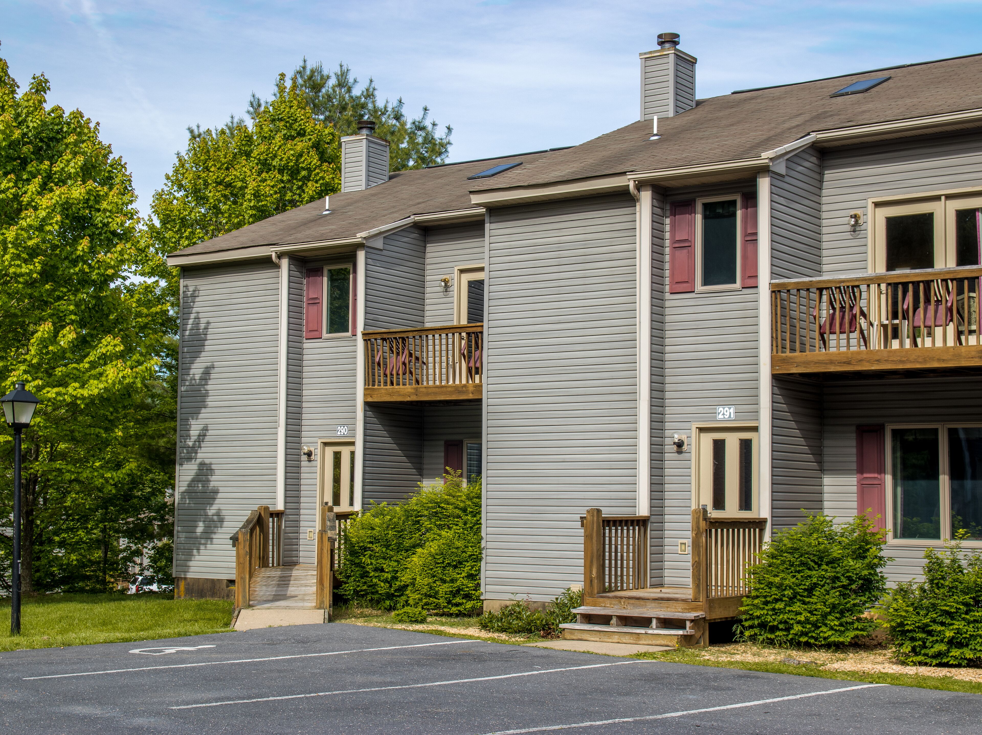 A two-story building with a gray exterior, a wooden balcony on the second floor, and a small front porch.