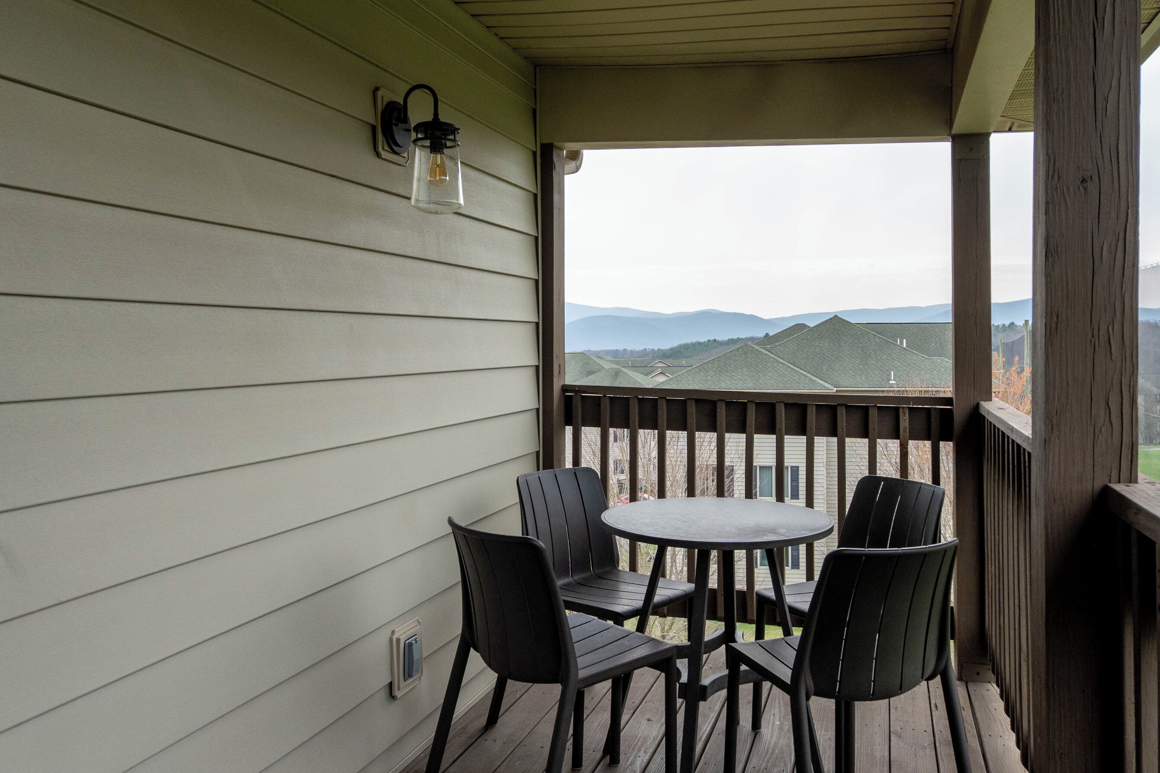 A covered outdoor area with a table and chairs, a view of distant mountains, and a wooden railing.