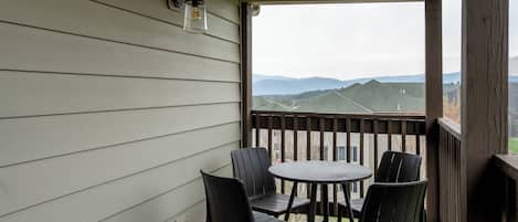 A covered outdoor area with a table and chairs, a view of distant mountains, and a wooden railing.