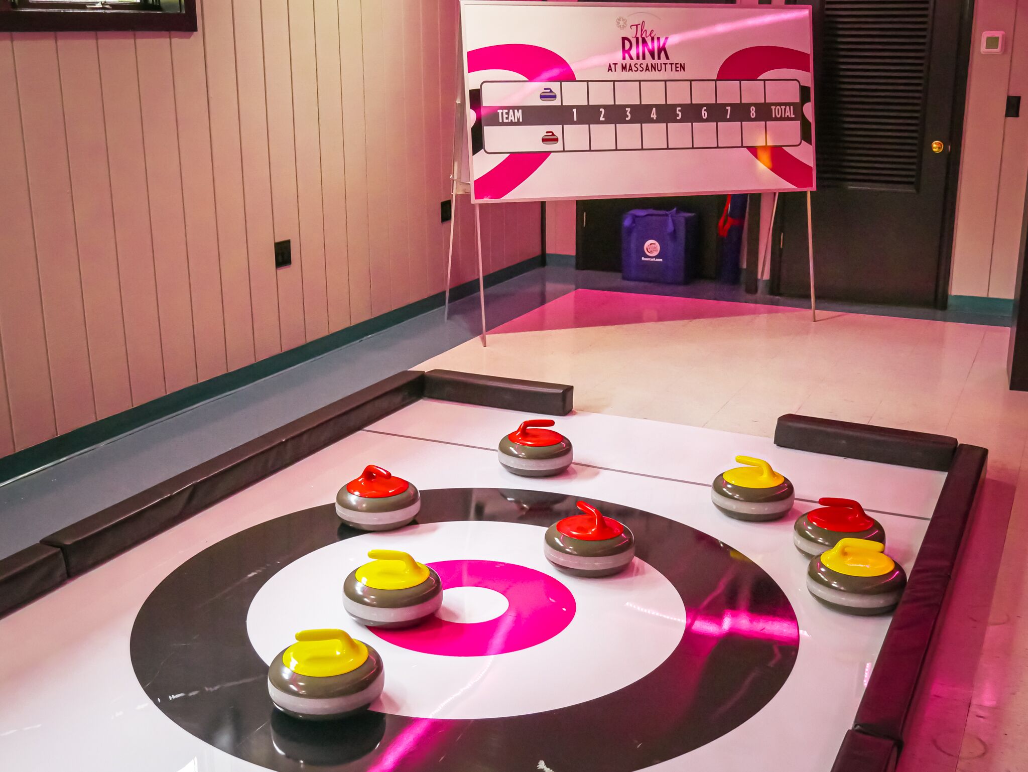 Pista de curling com pedras de curling dispostas em círculo, placar e faixa com a inscrição 'The Rink at Massanutten'.