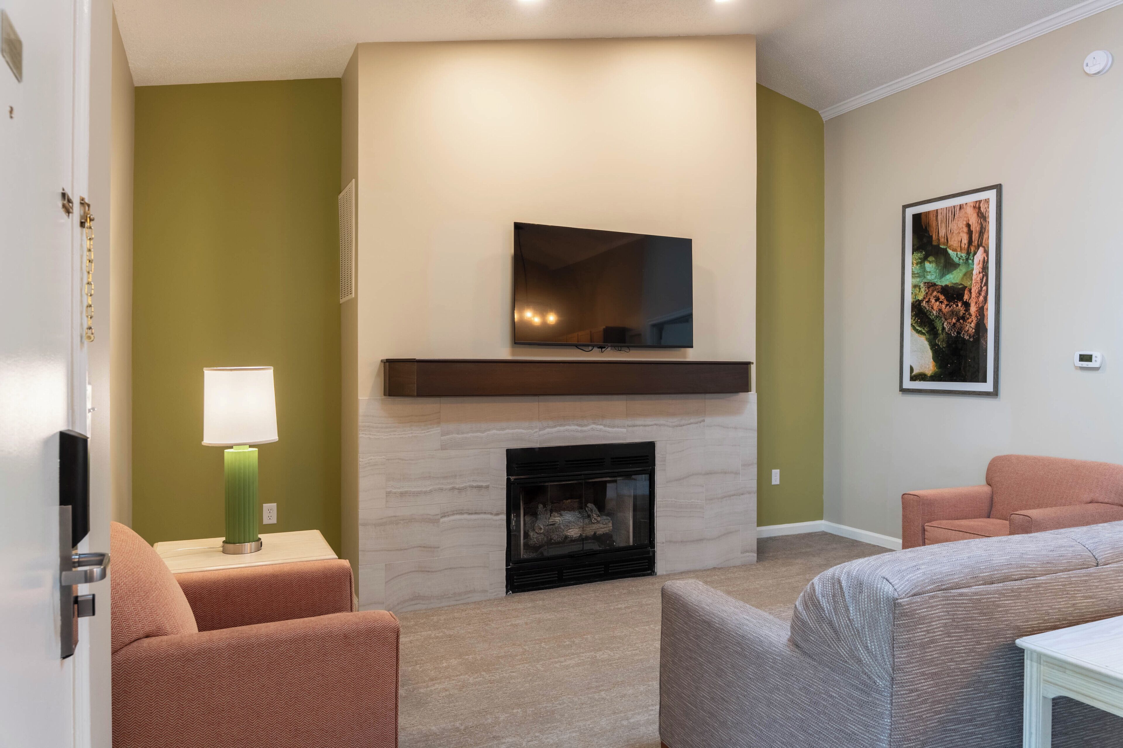 Una sala de estar con chimenea, un televisor montado encima y un cuadro en la pared.