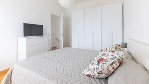 Un dormitorio con cama, televisor en una cómoda, armario y lámpara colgante.