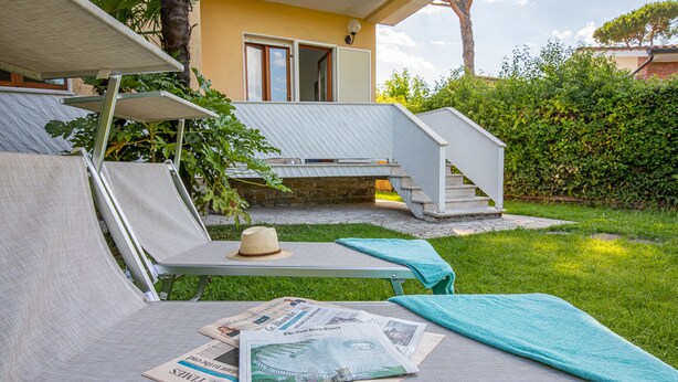 Un espacio al aire libre con sol, sillones de descanso, un sombrero y periódicos.
