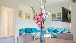 Un comedor con una mesa de madera, un florero con flores y un sofá con cojines azules al fondo.