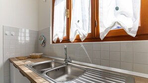 Una cocina con dos lavamanos de acero inoxidable, una encimera de madera y un ventanal con cortinas blancas.