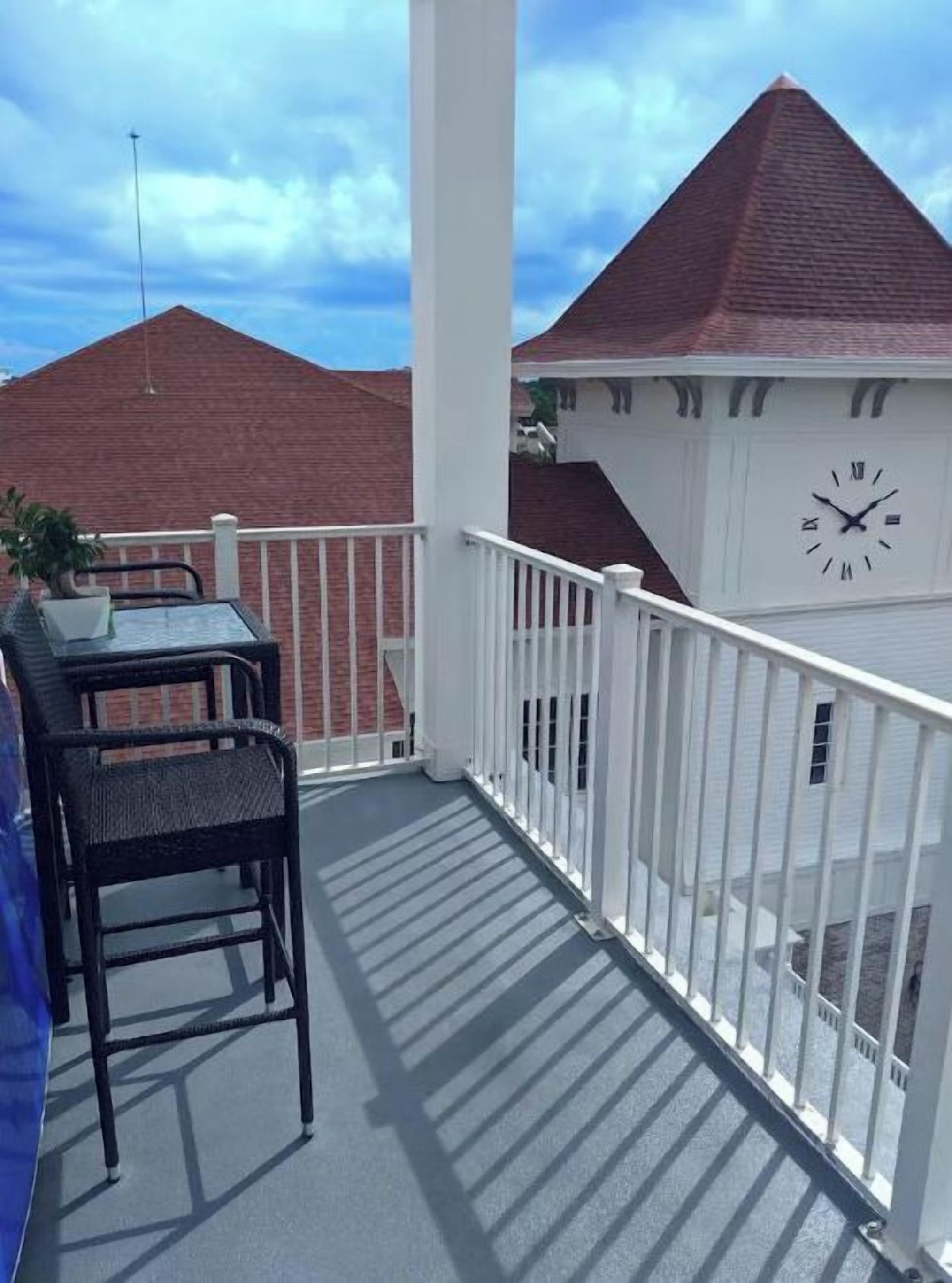 Ein Balkon mit Tisch und Stühlen, einer Uhr und Blick auf ein Gebäude mit rotem Dach.