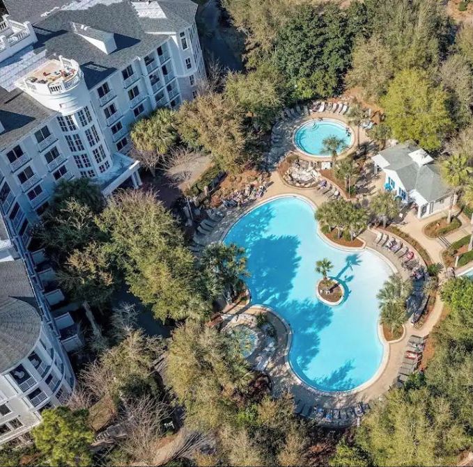 An aerial view of a resort with multiple swimming pools surrounded by trees and a large building with balconies.