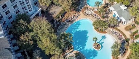 An aerial view of a resort with multiple swimming pools surrounded by trees and a large building with balconies.
