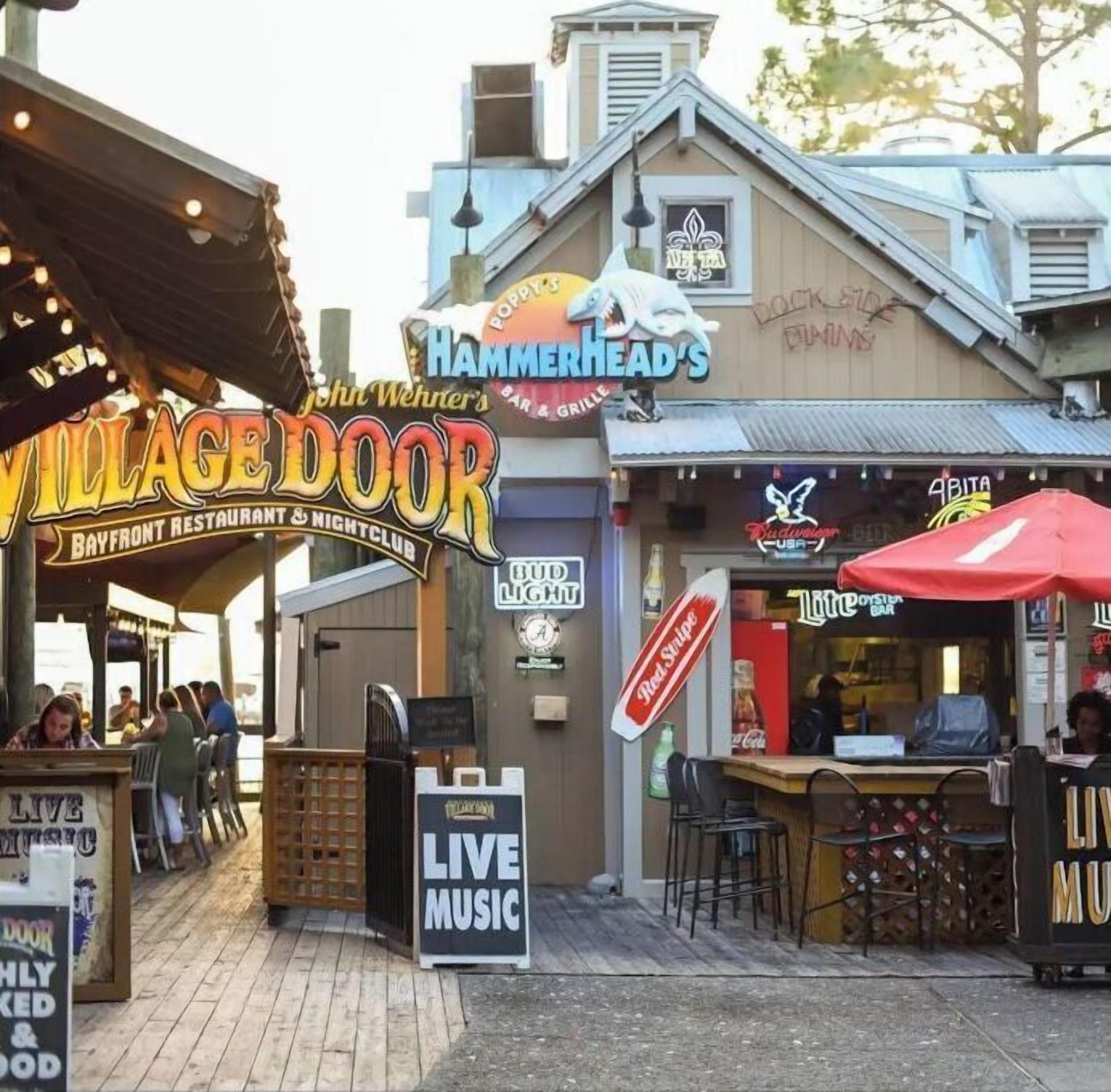 A bayfront restaurant and nightclub with outdoor seating, a live music sign, and various bar signs including Budweiser and Red Stripe.