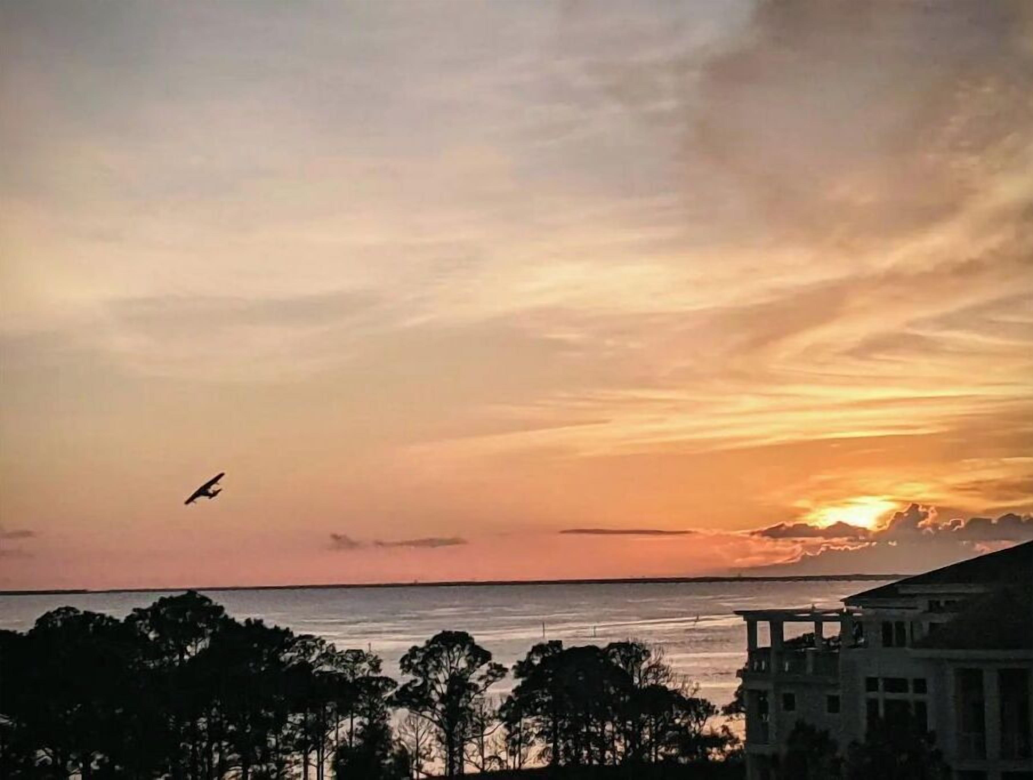Un tramonto su uno specchio d'acqua, con la sagoma di alberi e un edificio in primo piano.