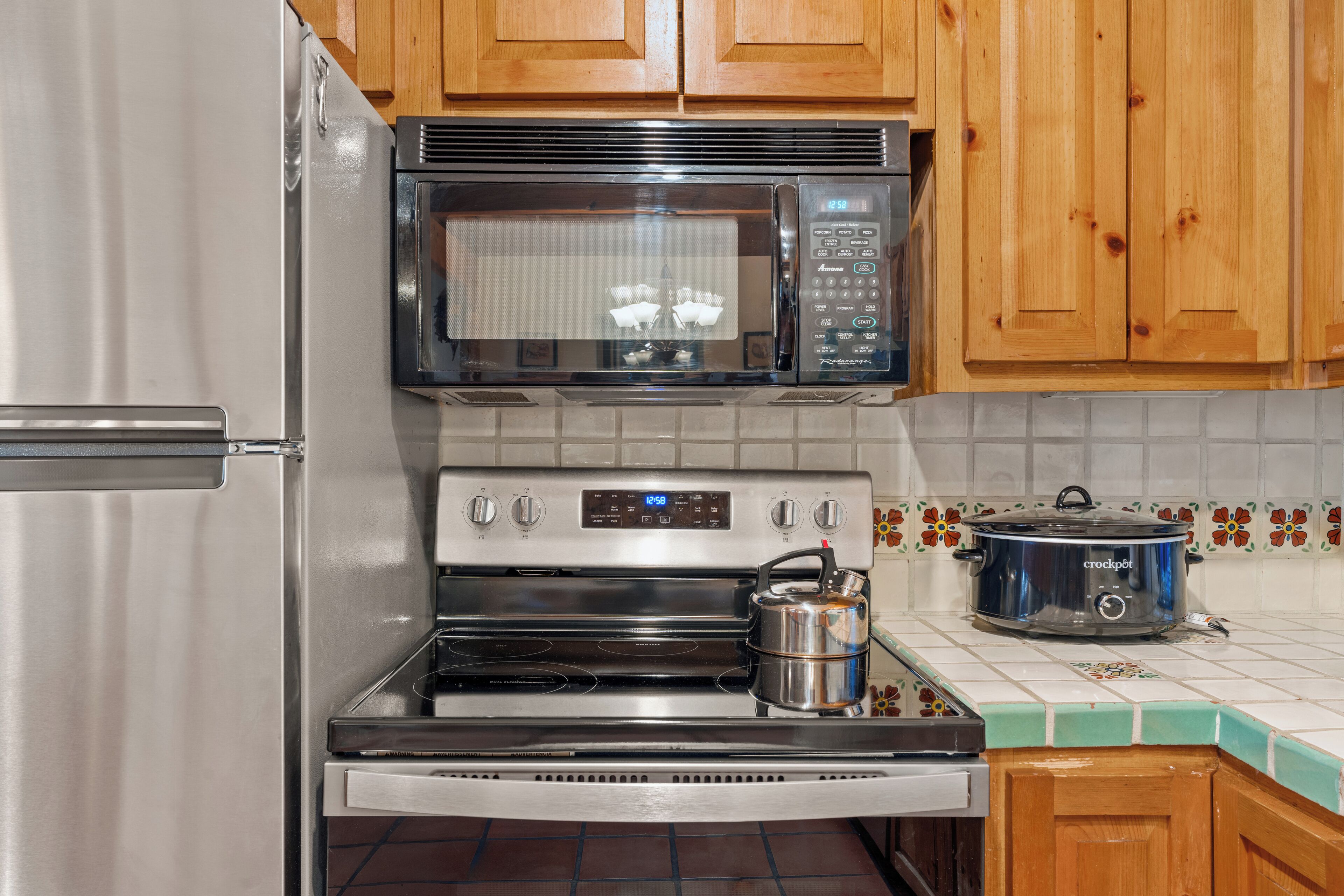 A kitchen with stainless steel appliances, including a refrigerator, microwave, oven, and a slow cooker.