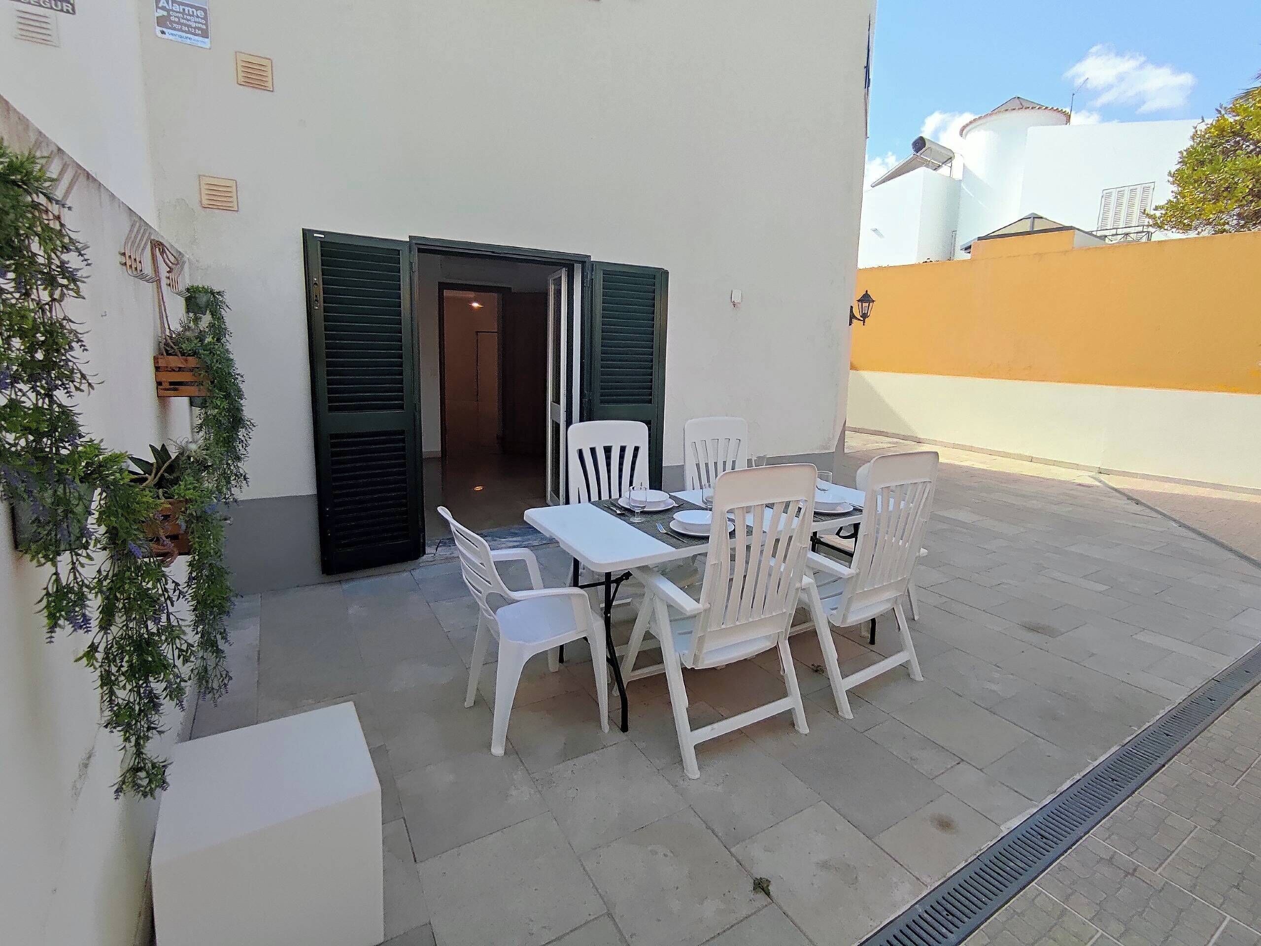 A patio with a table and chairs, a potted plant, and a building entrance with shutters.
