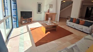 Ein geräumiges Wohnzimmer mit großem Fernseher, Kamin, einer Couch und einer Treppe zu einer weiteren Ebene.