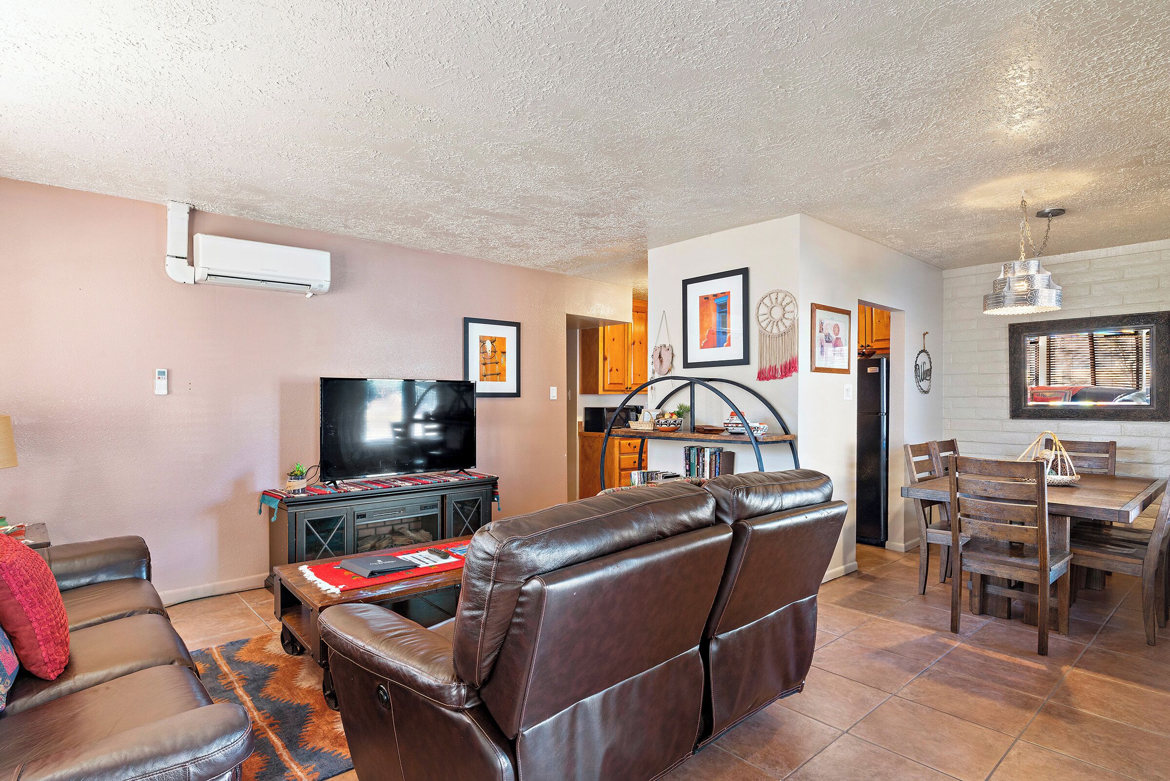 A living room with a leather sofa, a TV, and a dining area with wooden chairs and a table.