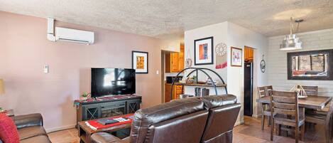 A living room with a leather sofa, a TV, and a dining area with wooden chairs and a table.