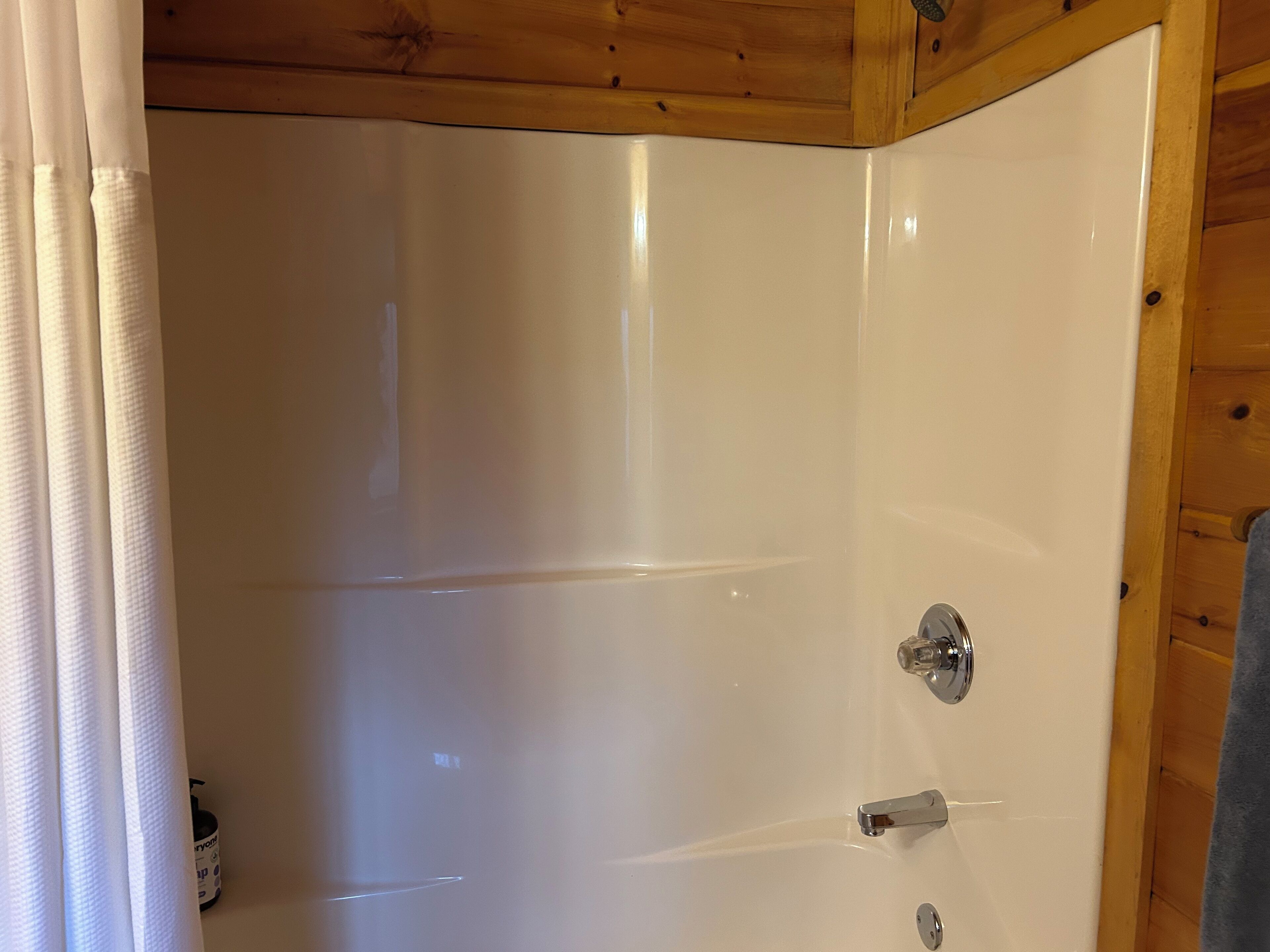 A bathroom with a white door, a shower, and a wooden ceiling.