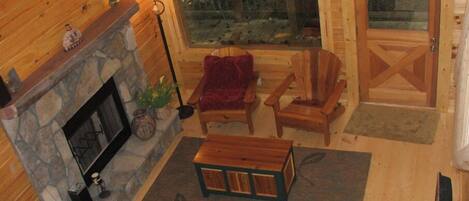 Interior acogedor de una cabaña con chimenea de piedra, muebles de madera y un ventanal con vistas al exterior.