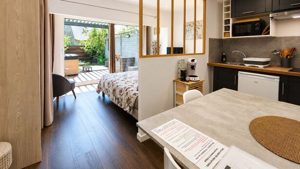 A compact kitchen with modern appliances, a dining area with a table, and a bedroom with a bed and a view to an outdoor patio.