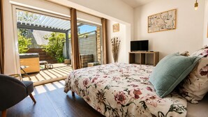 A bedroom with a bed, a TV, a chair, and a view of the outdoors.