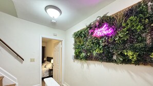 A hallway with a staircase, a neon sign, and a wall with various plants. - Downtown Home - Close to Topgolf, Ravens Stadium, Orioles Park, UM Baltimore (Baltimore)