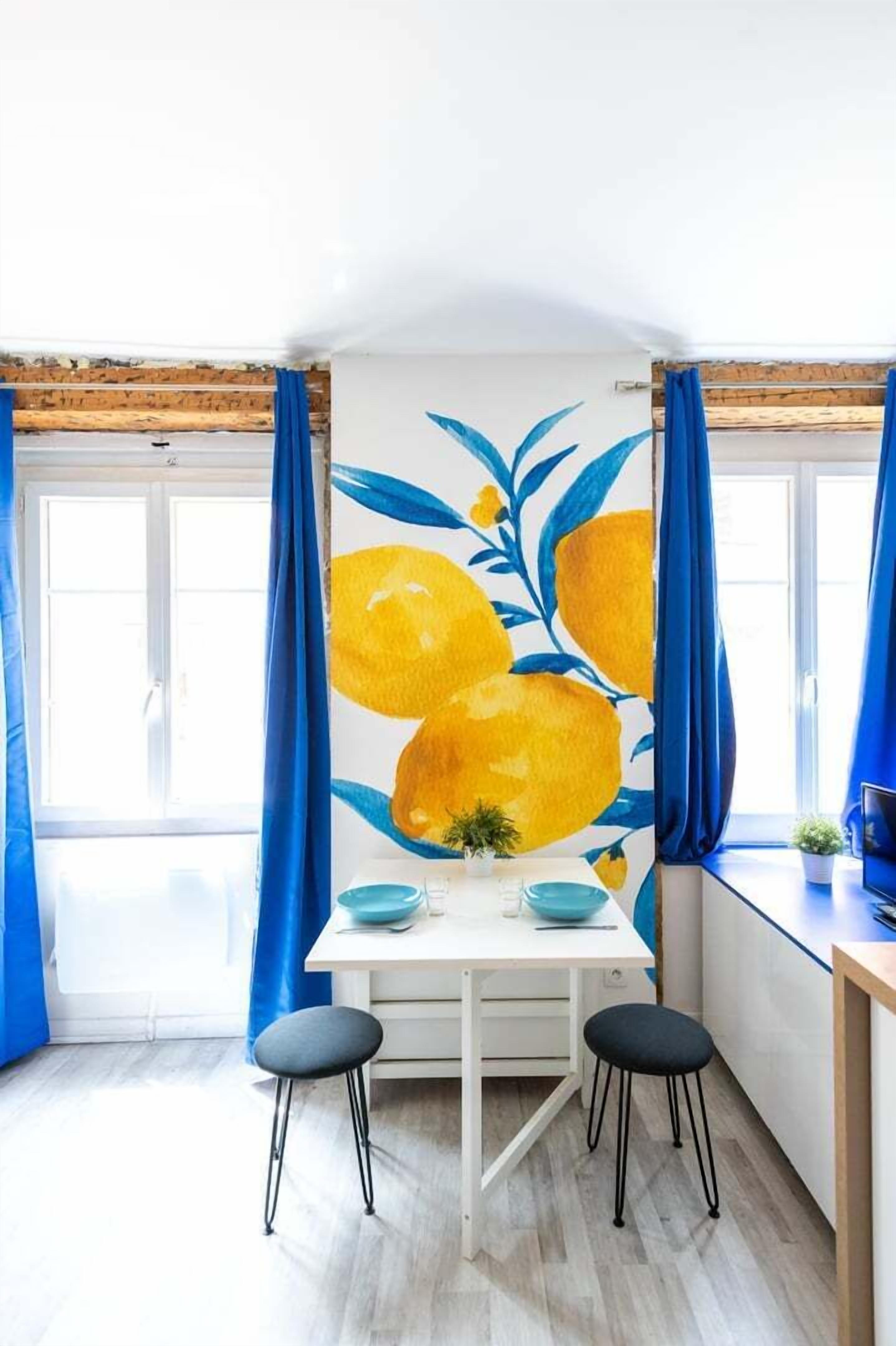 A dining area with a white table, two black stools, and a blue curtain.