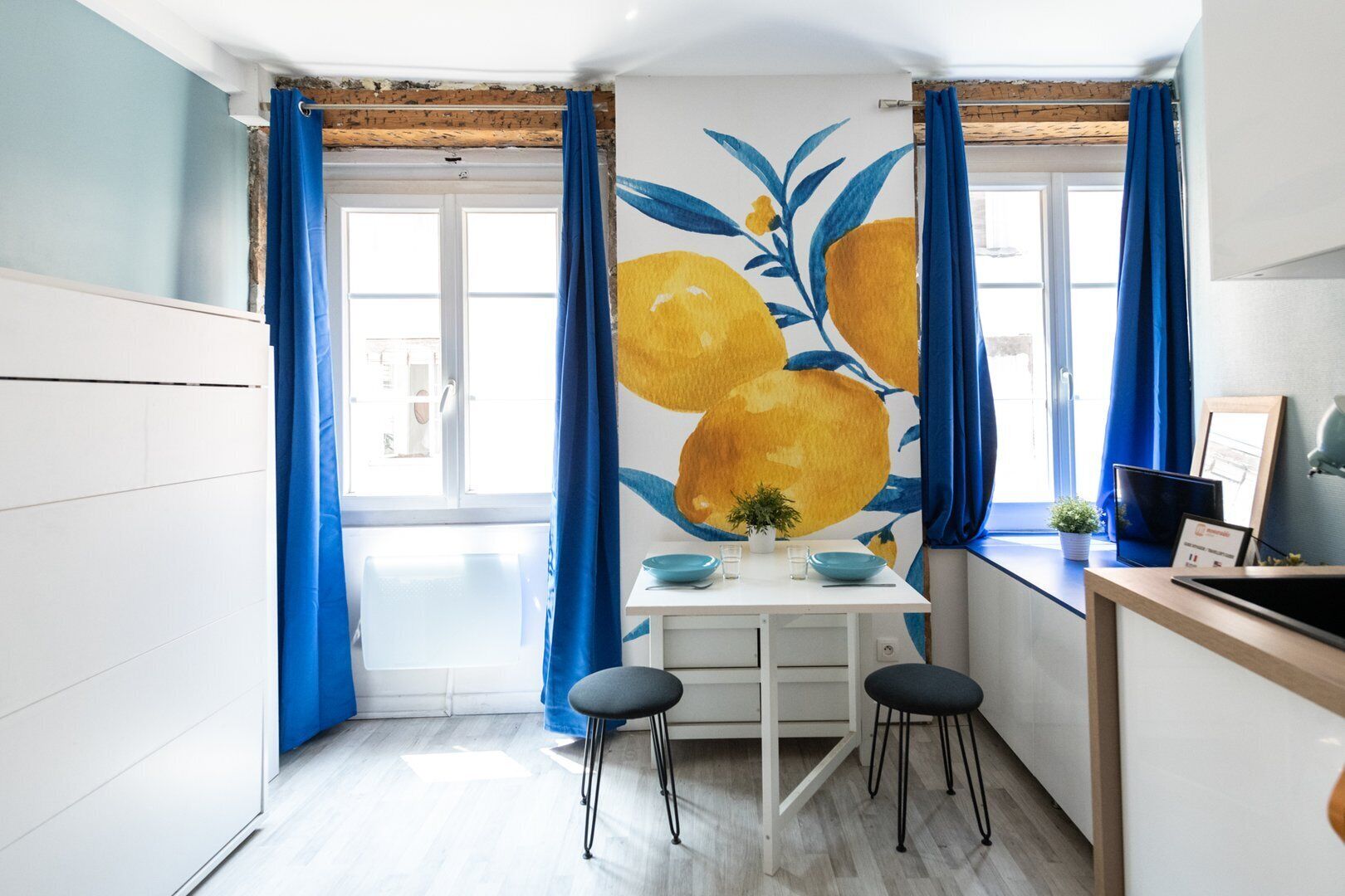 Una cocina moderna con encimera blanca, cortinas azules y un amplio ventanal.