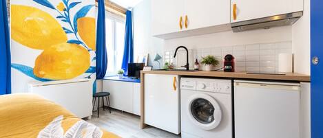 Cocina compacta con lavadora, lavamanos y encimera con varios objetos.