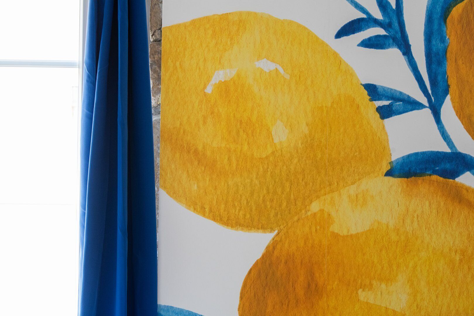 A window with blue curtains and a painting of yellow and blue abstract shapes.