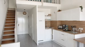 Una cocina moderna con muebles blancos, una escalera de madera y una pequeña zona de comedor.