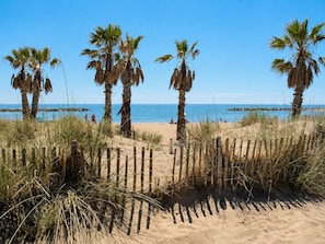 Una playa con palmeras, una valla de madera y el océano al fondo.