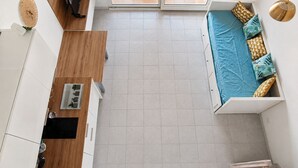 Un espacio habitable compacto con kitchenette, comedor y cama con almohadones estampados.