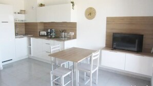 Una cocina moderna con armarios blancos, una mesa de comedor de madera y un televisor de pantalla plana.