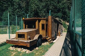 A brick structure with a chimney, a wheel, and a ladder, surrounded by a green fence and trees. - Charming chalet for 8 people, 3 BD, 2 BT, kitchen (Zvolen)