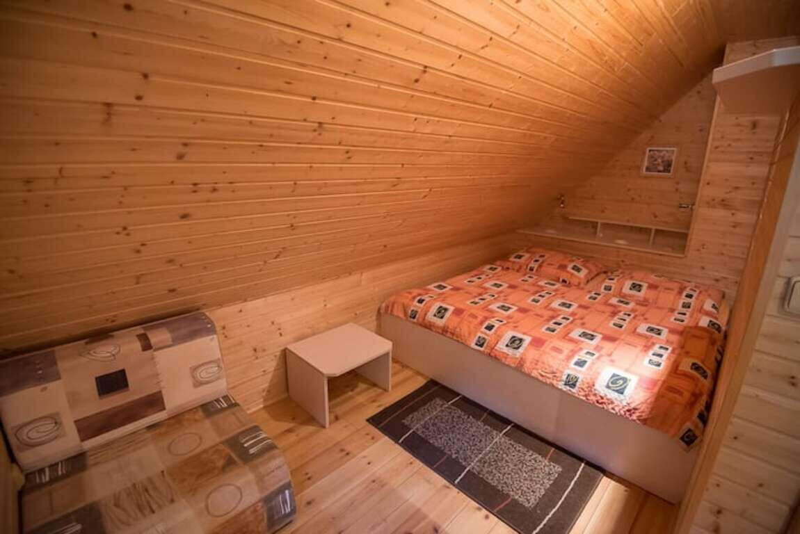 Una habitación pequeña y acogedora con techo inclinado de madera, una cama con colcha estampada, una mesita de noche y una alfombra en el suelo.
