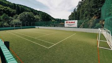 An outdoor tennis court with a net, surrounded by a green fence and trees.