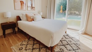 Un dormitorio con una cama grande, dos mesitas de noche con lámparas, un tapete estampado y vistas a una piscina a través de un ventanal.