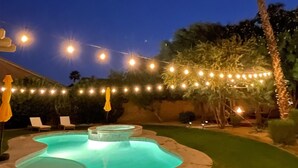 Un patio trasero con piscina, luces colgantes y una palmera.