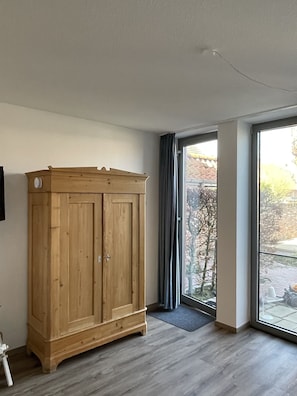 Una habitación con un armario de madera, un gran ventanal corredero que da a un espacio exterior y un piso de baldosas grises.