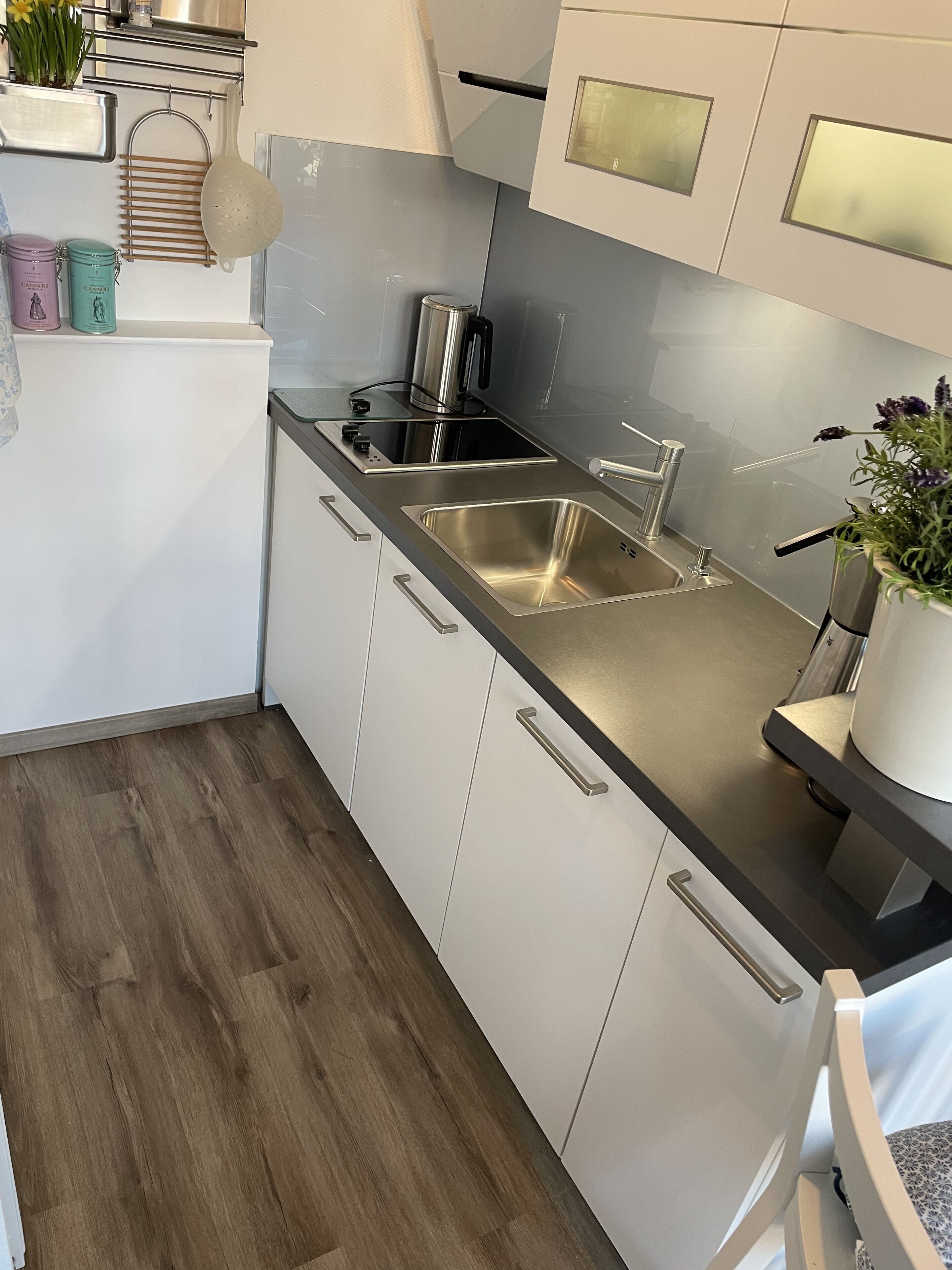 Cocina moderna con electrodomésticos de acero inoxidable, muebles de color blanco y piso de madera.