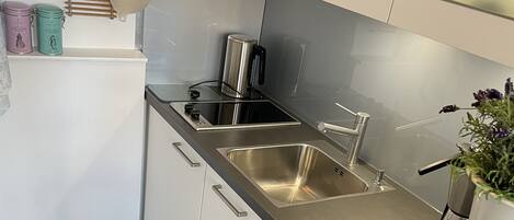 Cocina moderna con electrodomésticos de acero inoxidable, muebles de color blanco y piso de madera.