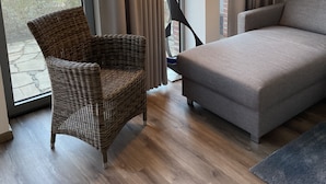 A modern room with a grey sofa, wicker chair, and a large window with curtains.