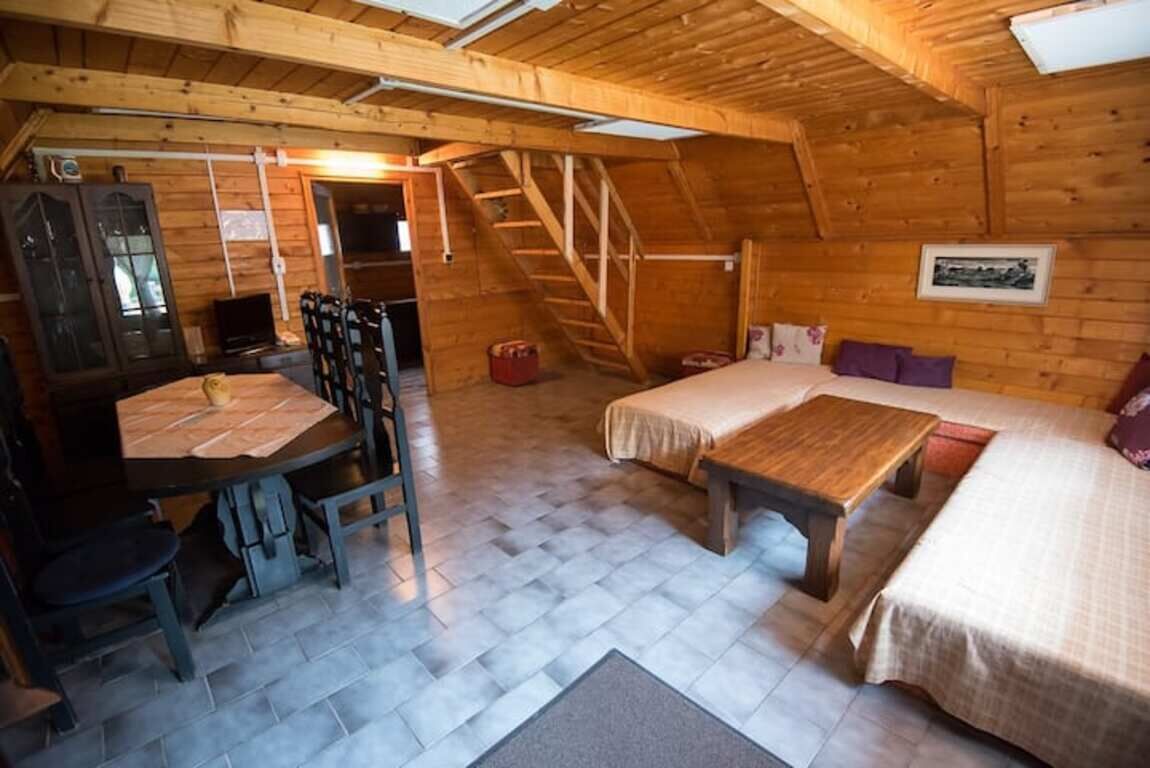 A cozy attic room with a wooden floor, a bed, a desk with a chair, and a staircase.